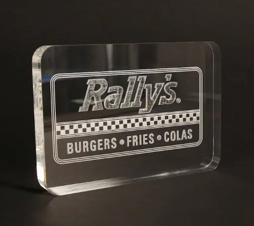 Favism3D: Grabado láser de alta precisión en acrílico para carteles, señalización y displays personalizados. Cartel de acrílico transparente con logo de 'Rally's' grabado con láser, ideal para señalización comercial o displays.