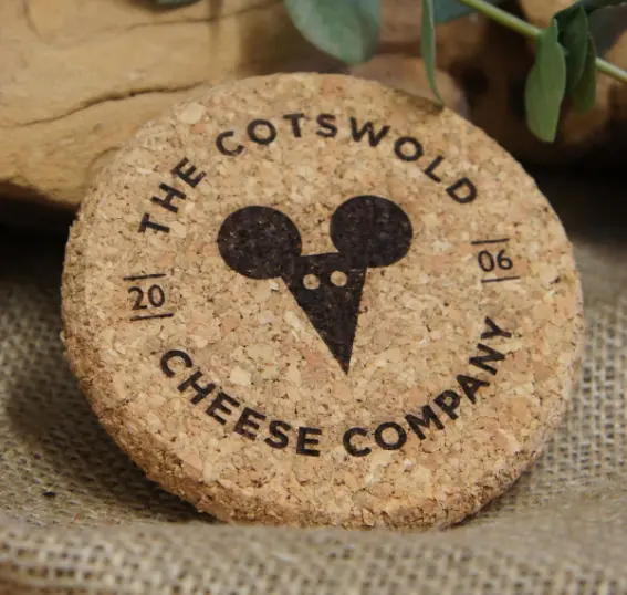 Favism3D: Grabado láser en corcho para posavasos personalizados, merchandising y regalos corporativos. Posavasos de corcho redondo con logo 'The Cotswold Cheese Company' grabado con láser, ideal para regalos personalizados.