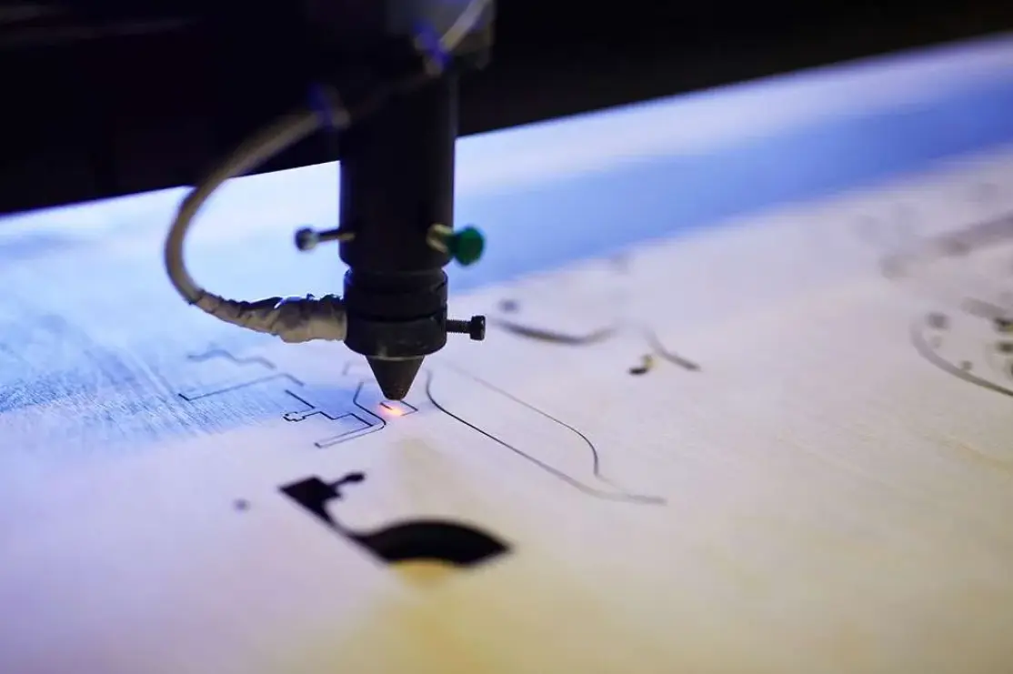 Favism3D: Grabado y corte láser con resultados limpios, precisos y máxima eficiencia. Cabezal láser grabando con precisión sobre madera clara, creando líneas limpias y detalladas de forma eficiente.