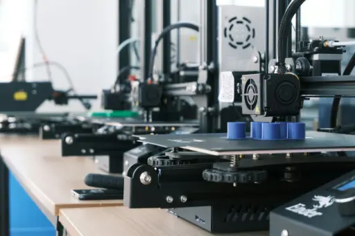 Fotografía artística de una impresora 3D imprimiendo en filamento naranja, ideal para ilustrar la tecnología maker.