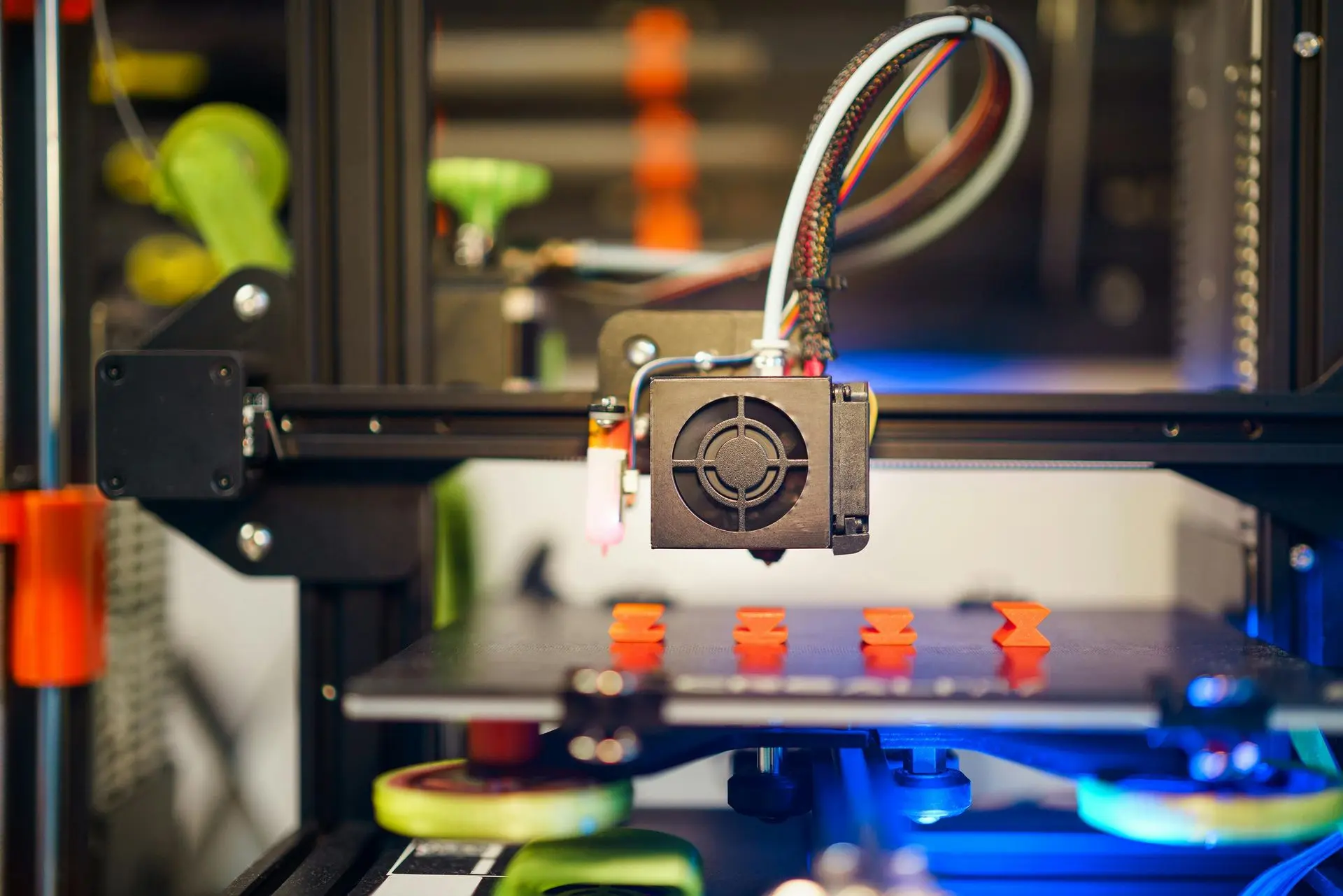 Vista frontal de una impresora 3D en funcionamiento mostrando piezas impresas con una primera capa uniforme gracias a la nivelación automática de cama.