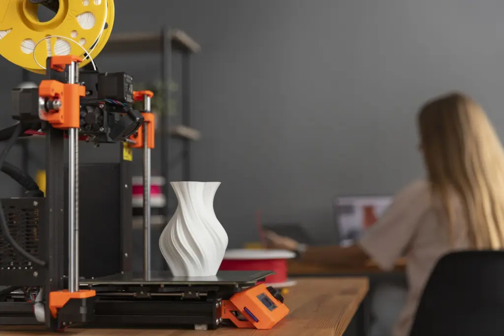 Fotografía de una impresora 3D imprimiendo un jarrón decorativo en un entorno de oficina, ideal para ilustrar guías sobre impresión 3D silenciosa y en espacios de trabajo.