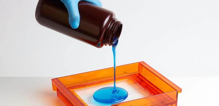 Mano vertiendo resina azul en la cuba de una impresora 3D SLA, mostrando el material para impresión de alta resolución.